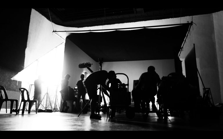 Behind the shooting of video online commercial production and film crew team working and setting light or camera or soft box and equipment set up in big studio in silhouette style