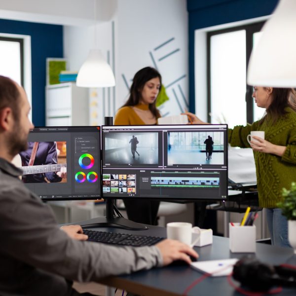 Video maker editing movie using post production software working in creative start up agency office with two monitors. Videographer processing audio film montage on computer in multimedia company